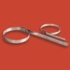 Two stainless steel cable ties, one larger than the other, with adjustable fasteners and extended tails, are shown on a solid red background. Perfect for use with a Stainless Steel Cable Marking Tag.